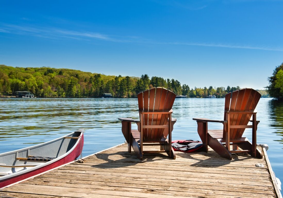 Two Adirondack chairs on a wooden dock on a lake in Muskoka, Ont